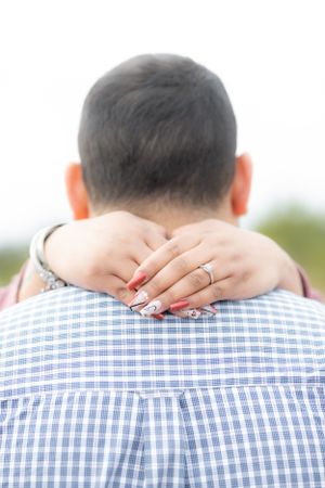 Close-up of engagement ring while couple embraces in checkered shirt.