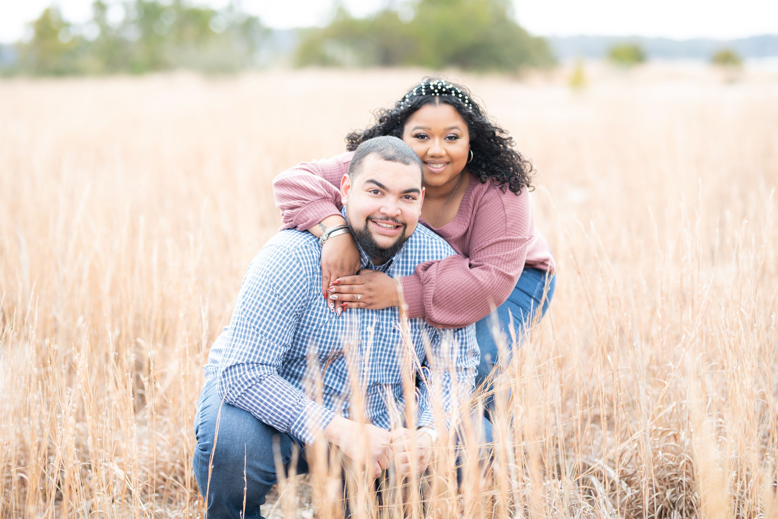 Joyful couple embracing in a golden wheat field during engagement photo session.
