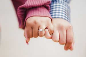Two hands with engagement rings intertwined wearing pink and blue sleeves.