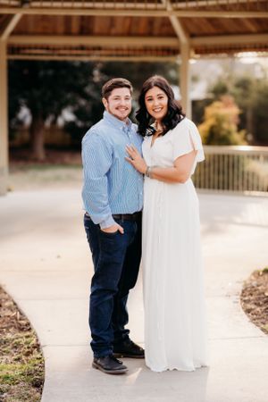 A couple poses together under a rustic pavilion during their engagement photo session.