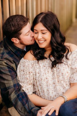 An intimate engagement photo showing a couple sharing a sweet moment against a beige backdrop.