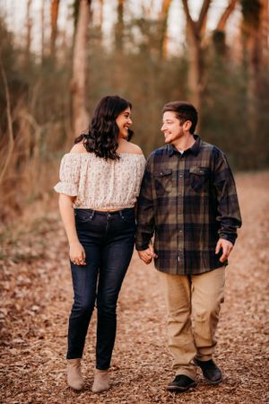 A couple shares a joyful moment while walking along a leaf-covered forest path during autumn.