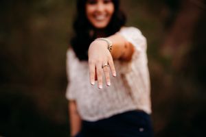 Close-up of an engagement ring being shown on an outstretched hand with a blurred background.