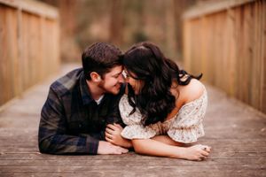 An intimate couple's portrait captured on a wooden bridge in a forest setting.