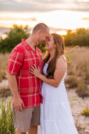 Intimate moment between couple in white dress and red plaid shirt during sunset photoshoot.