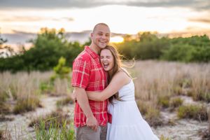 Happy couple embracing outdoors with golden sunset and tall grass in background.
