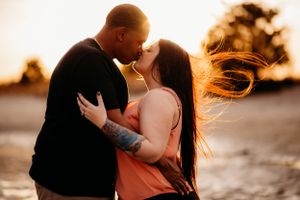 Sunset silhouette of couple embracing with hair blowing in golden light.