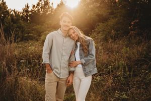 Couple shares intimate moment during golden hour photoshoot in rustic field setting.