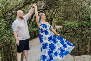 Dancing couple in blue floral dress and casual wear on woodland path.