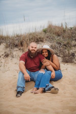 A casual couple relaxing together on sandy dunes during a beach photoshoot.