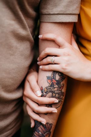 Close-up of hands showing engagement ring and tattoo against contrasting clothing.