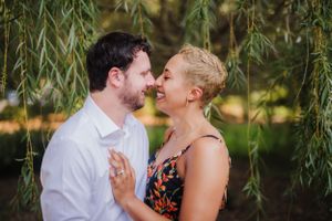 Romantic couple embracing under willow tree during summer photo session.