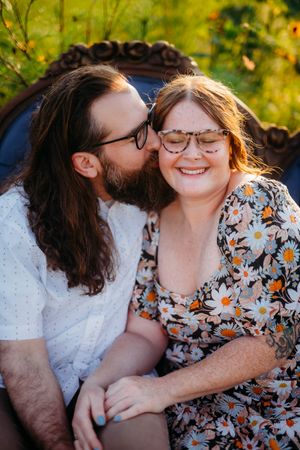 Couple in glasses share intimate moment while sitting outdoors in natural lighting.