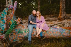 Engagement portrait of couple on vibrant painted fallen tree trunk in forest setting.