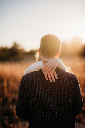 Back view of person in polka dot shirt with hands embracing during sunset photoshoot.