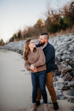 Couple sharing a tender moment on a rocky beach during golden hour.
