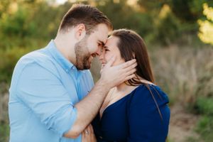 A tender romantic moment between a couple in coordinating blue outfits against a natural outdoor setting.