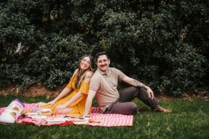 Couple relaxing on checkered blanket in lush garden setting.