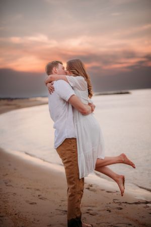 Romantic beach embrace during sunset with pink sky and shoreline in background.