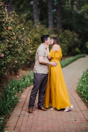 Intimate moment shared between couple on brick pathway surrounded by greenery.