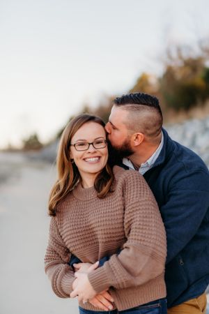 A couple in casual sweaters embracing during an outdoor engagement photoshoot.