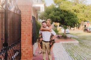 Couple enjoying playful moment by brick wall and iron gate during photo session.