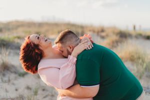 Joyful couple shares a playful moment on sandy dunes at sunset.