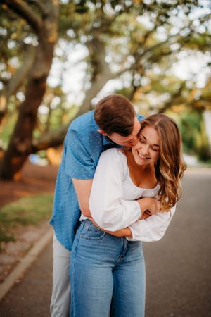 Couple sharing joyful moment on tree-lined path during golden hour.