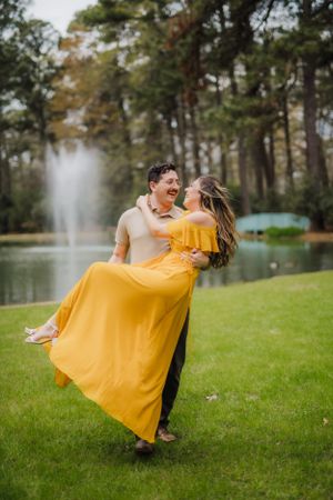 Joyful moment captured as couple spins on grass near lake with fountain.