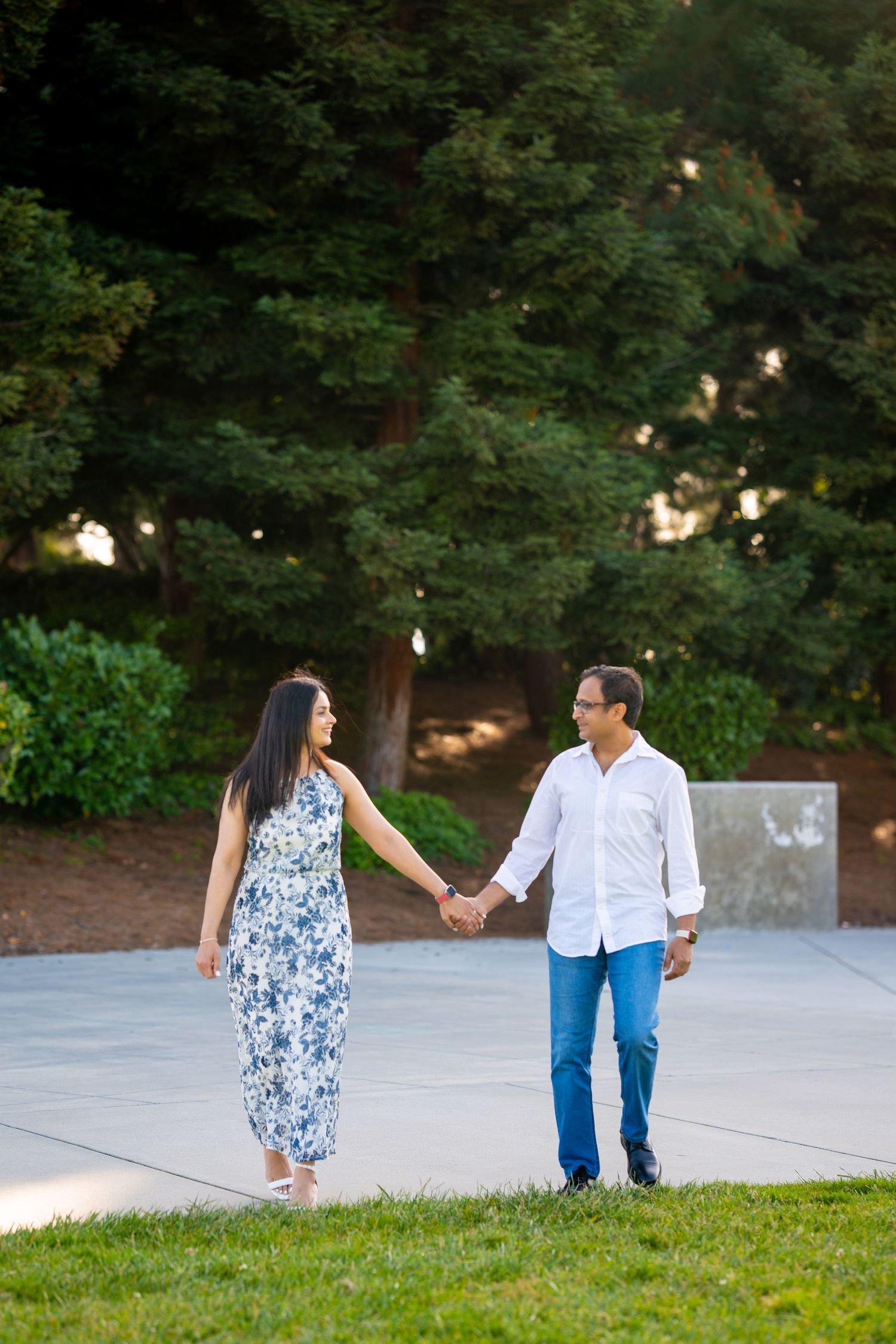 Couple holds hands while walking on path with trees in evening light.