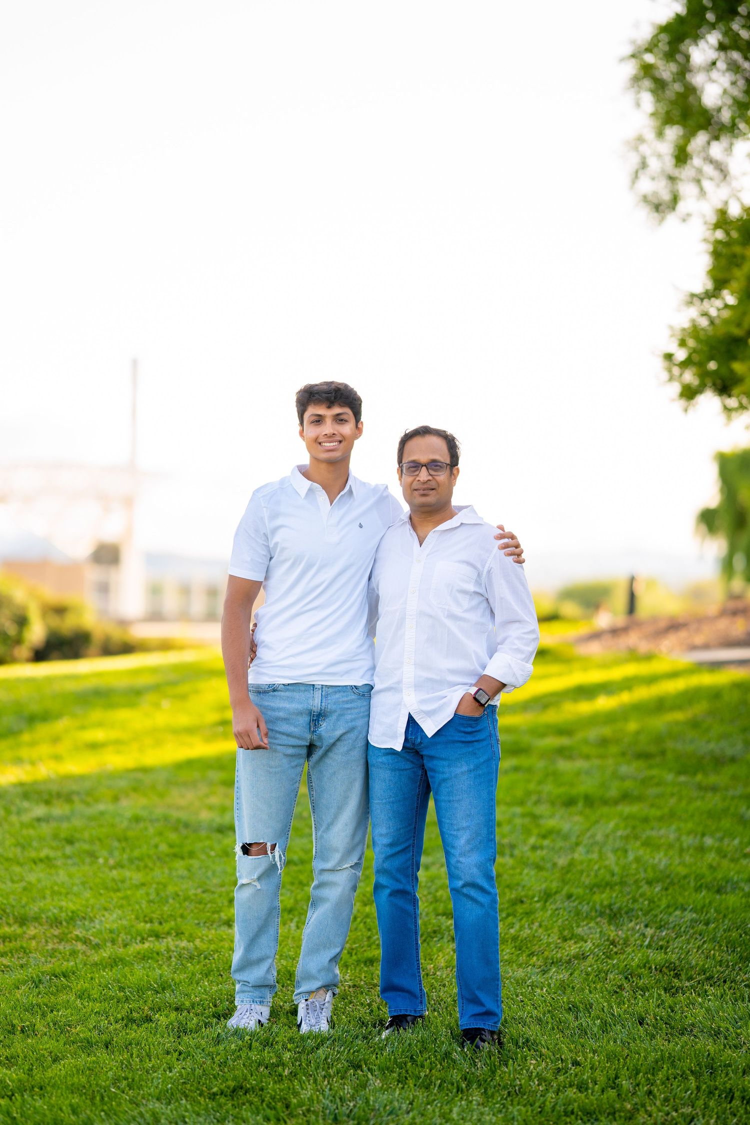 Two people stand together on grassy hill during golden hour outdoor photoshoot.