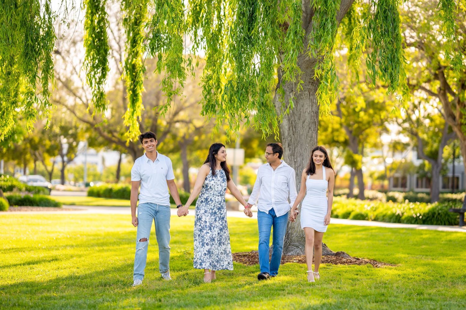 Family portrait under weeping willow tree in sunny park setting.