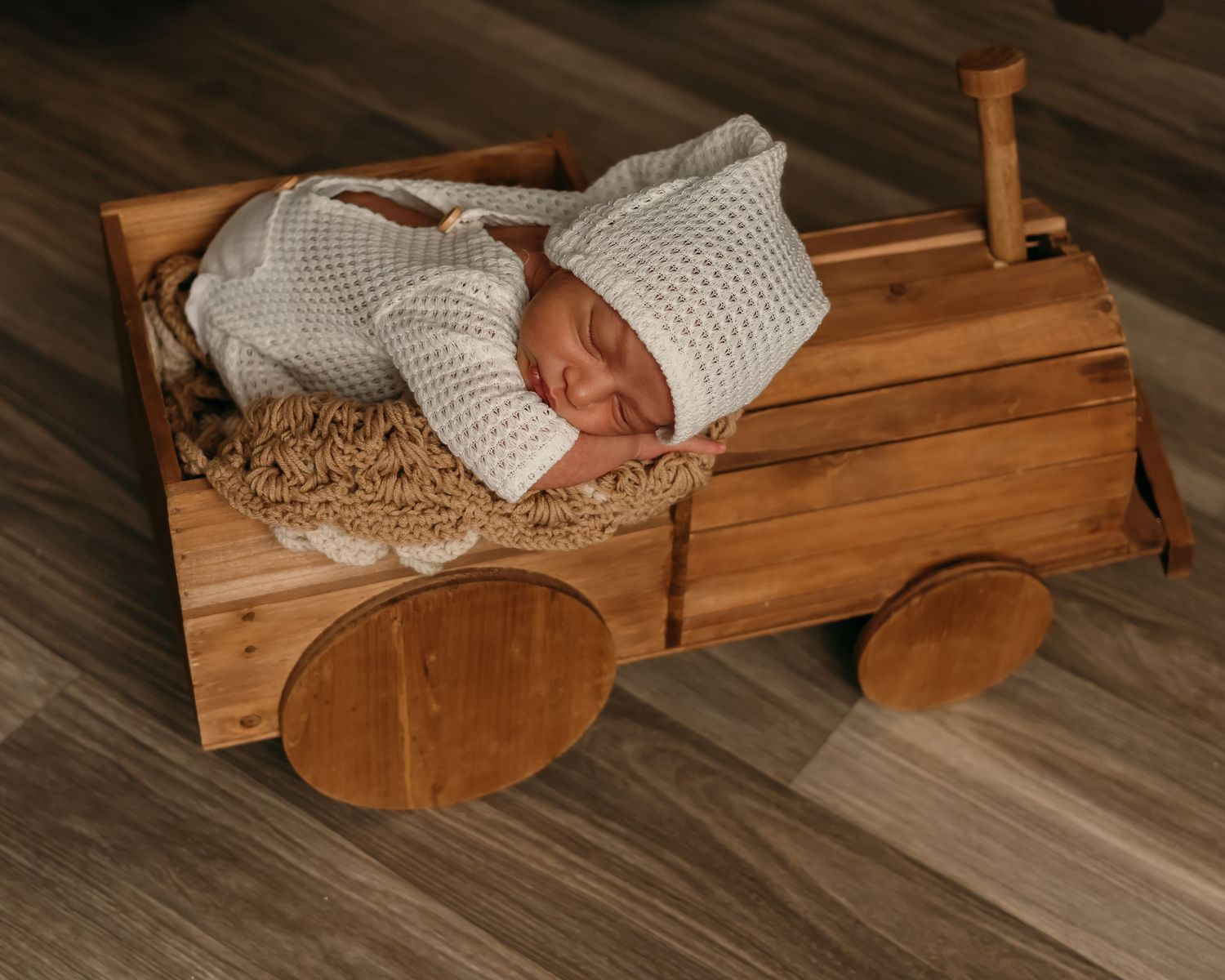 Newborn sleeping peacefully in wooden wagon with knitted white blanket.