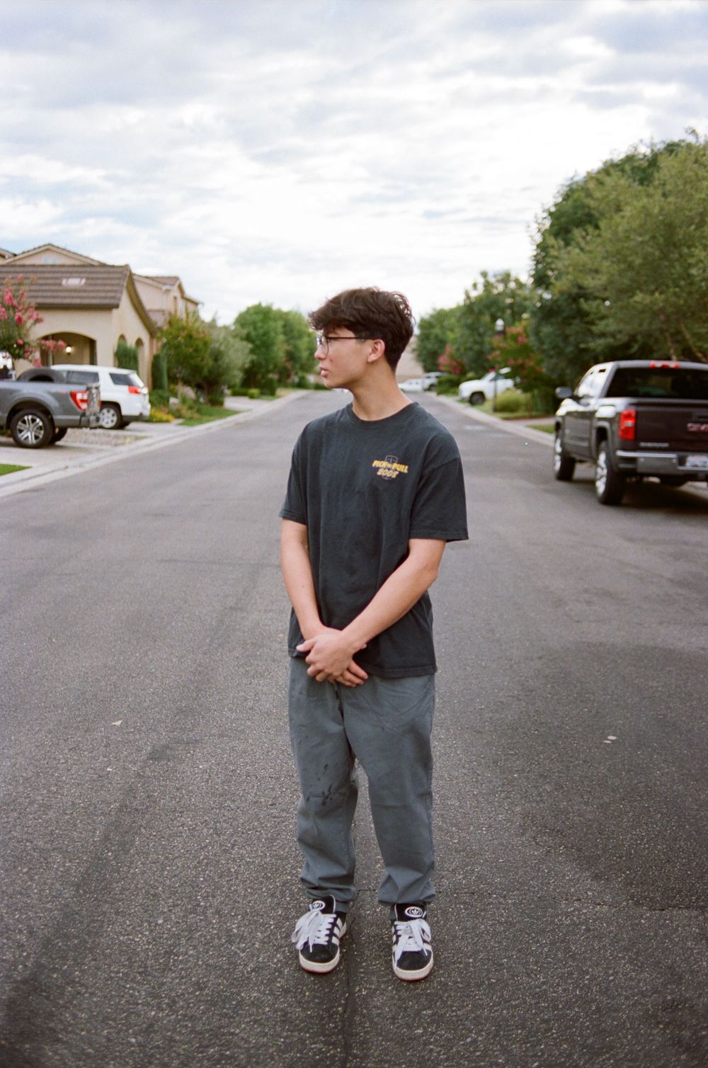 Person standing in middle of suburban street wearing dark t-shirt and jeans.