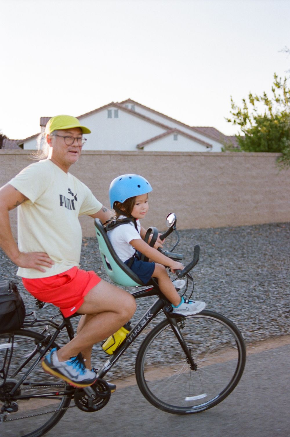 Cyclists on a bike equipped with child seat riding through a residential neighborhood.