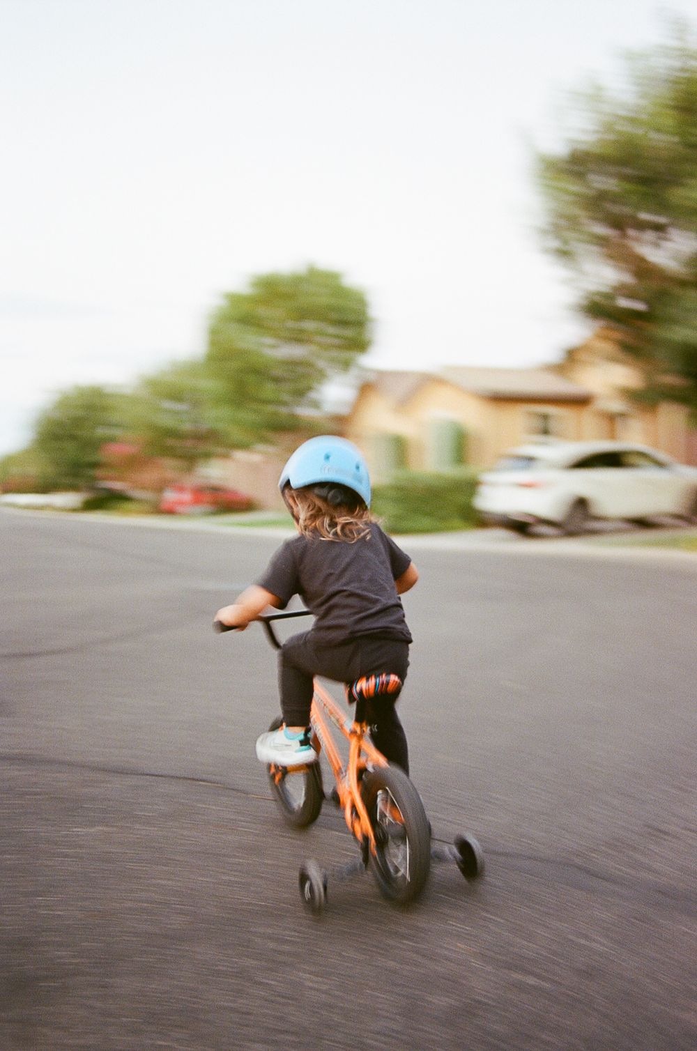 Child riding a bicycle with training wheels on a residential street.