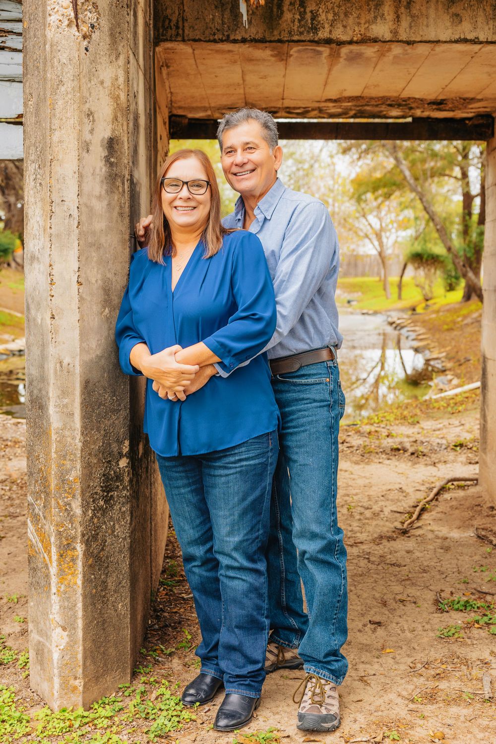 Couple posing together in a rustic outdoor setting with concrete pillars.