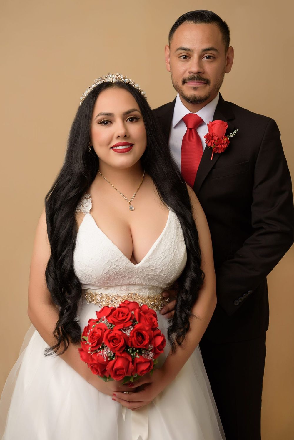 Wedding portrait with bride holding red rose bouquet and groom in black suit with red tie.