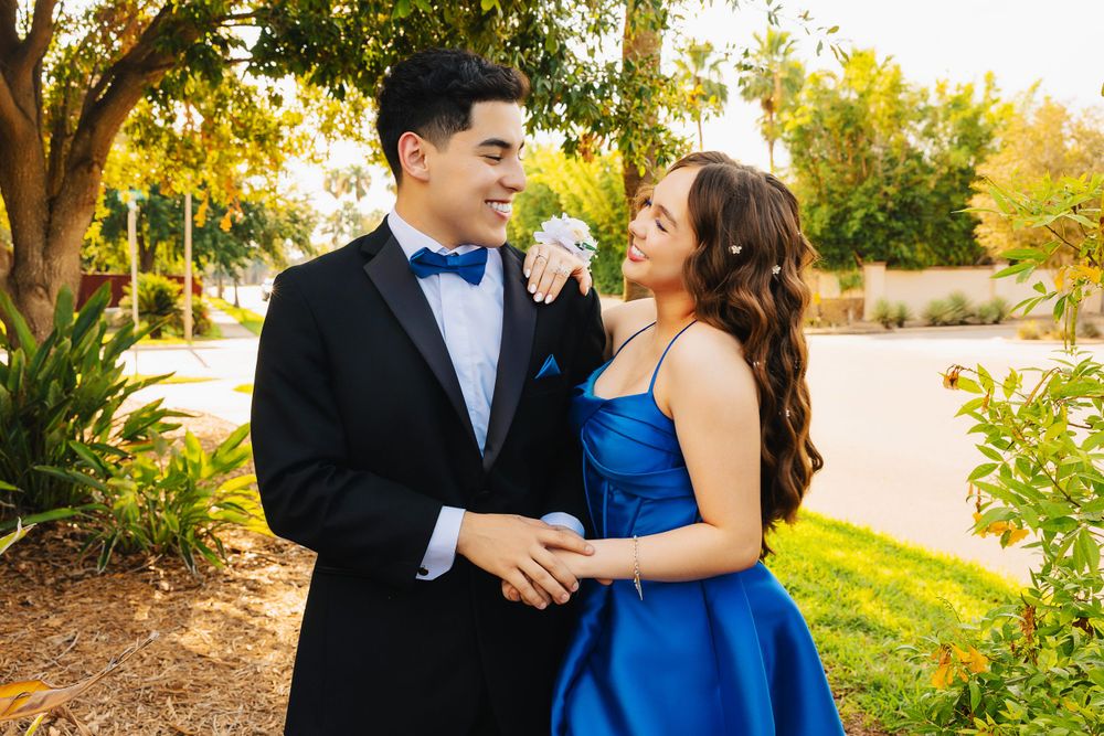 Couple in formal wear shares intimate moment in garden setting at dusk.