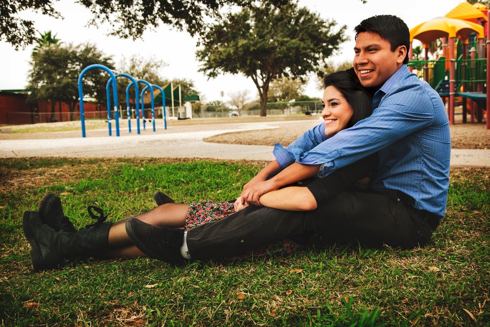 Couple relaxing together on grass with playground equipment in background.