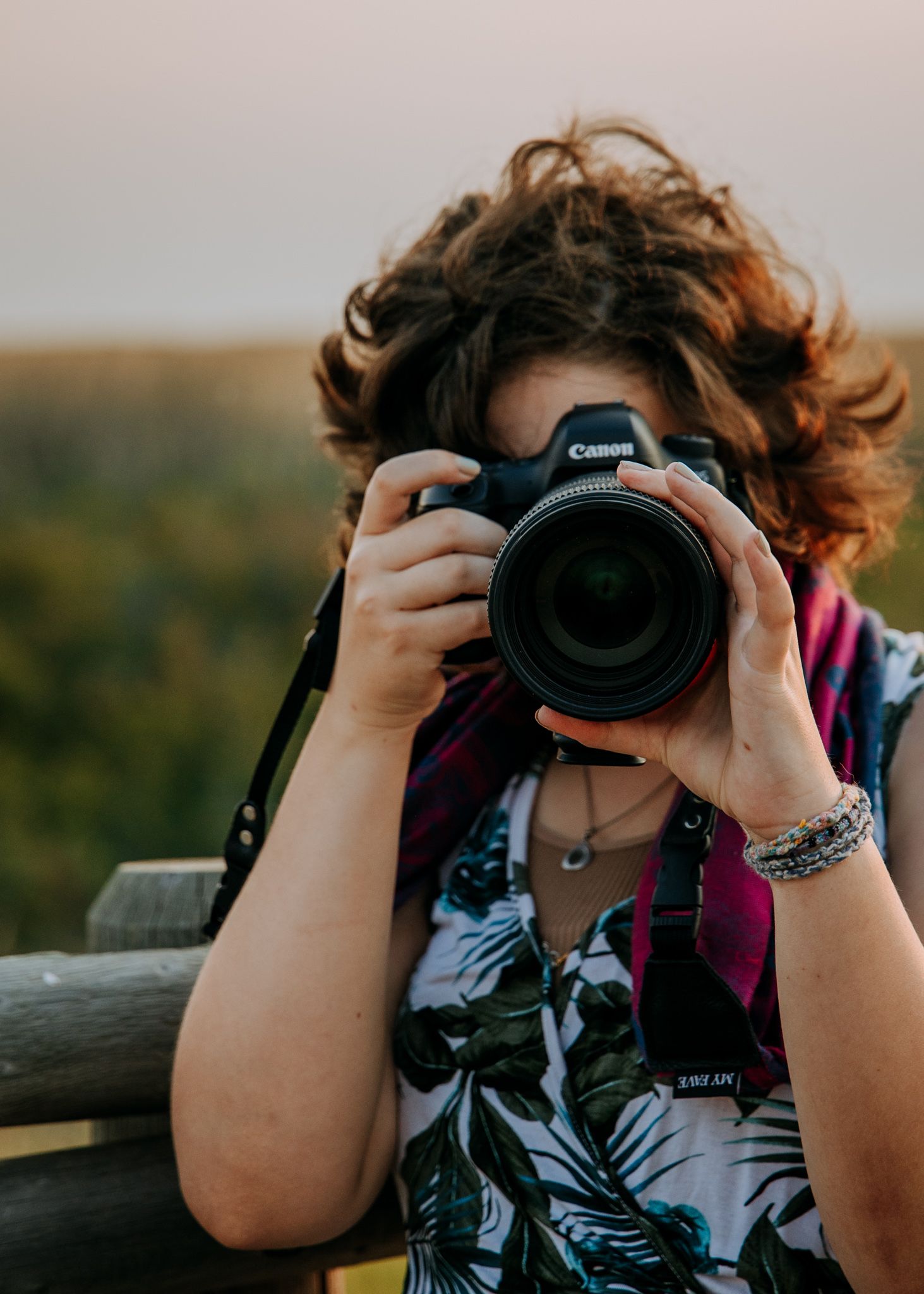 Photographer with curly hair holds Canon camera while taking pictures outdoors.