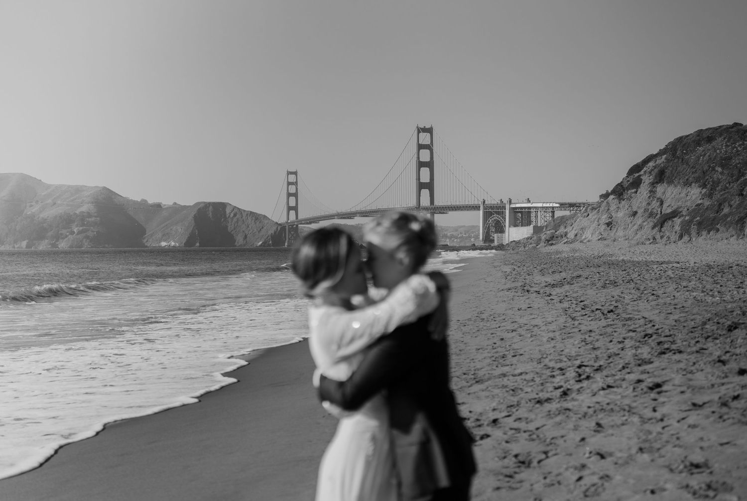 San Francisco Elopement Photographer - two brides are kissing on the beach with the Golden Gate Bridge behind them