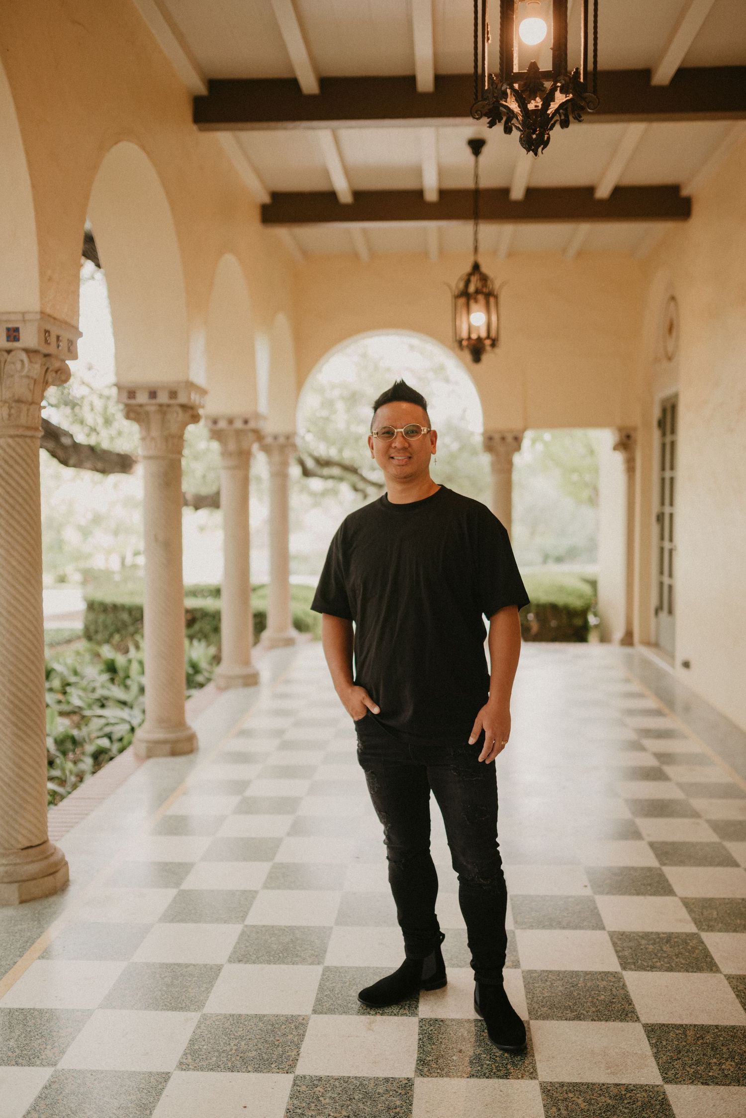 A photographer stands on a checkerboard floor under arched columns and hanging lanterns.