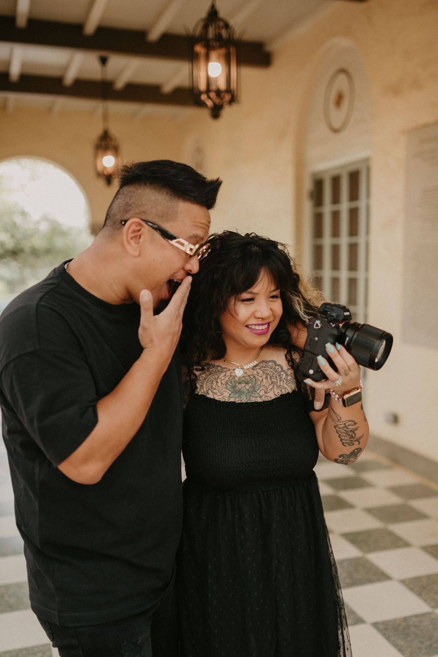 Two photographers review images together while standing in a covered outdoor colonnade.