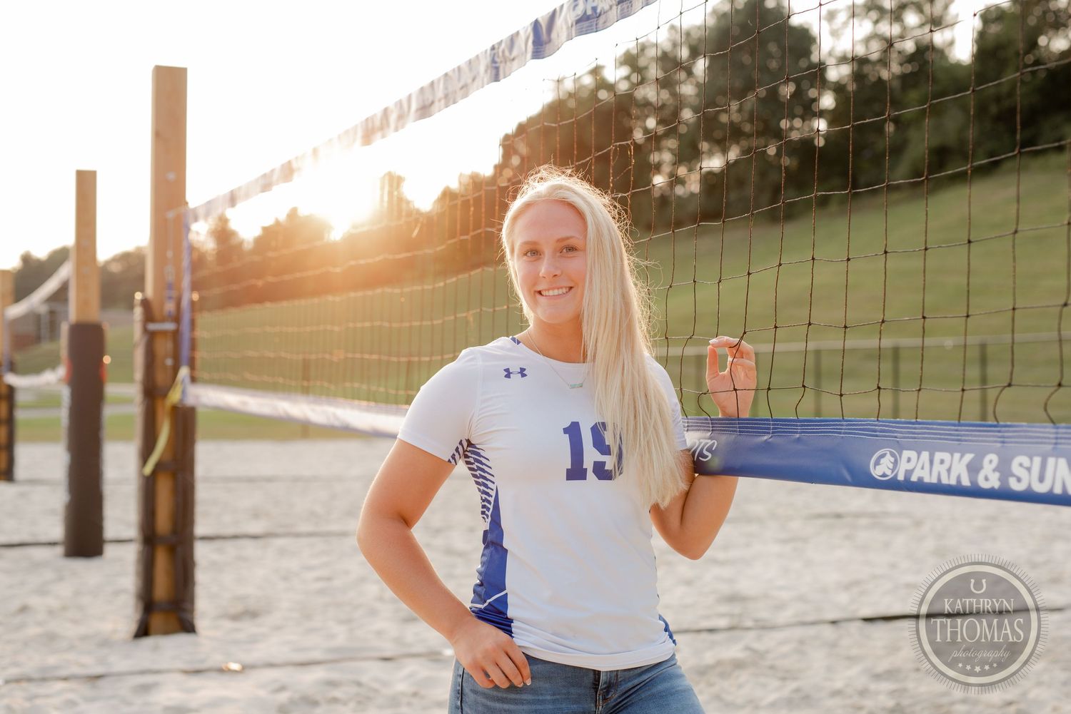 Athlete in blue and white uniform standing by volleyball net during sunset.