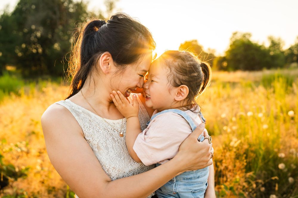 Mom hugging her toddler daughter in a field of daisies at sunset in Redmond.