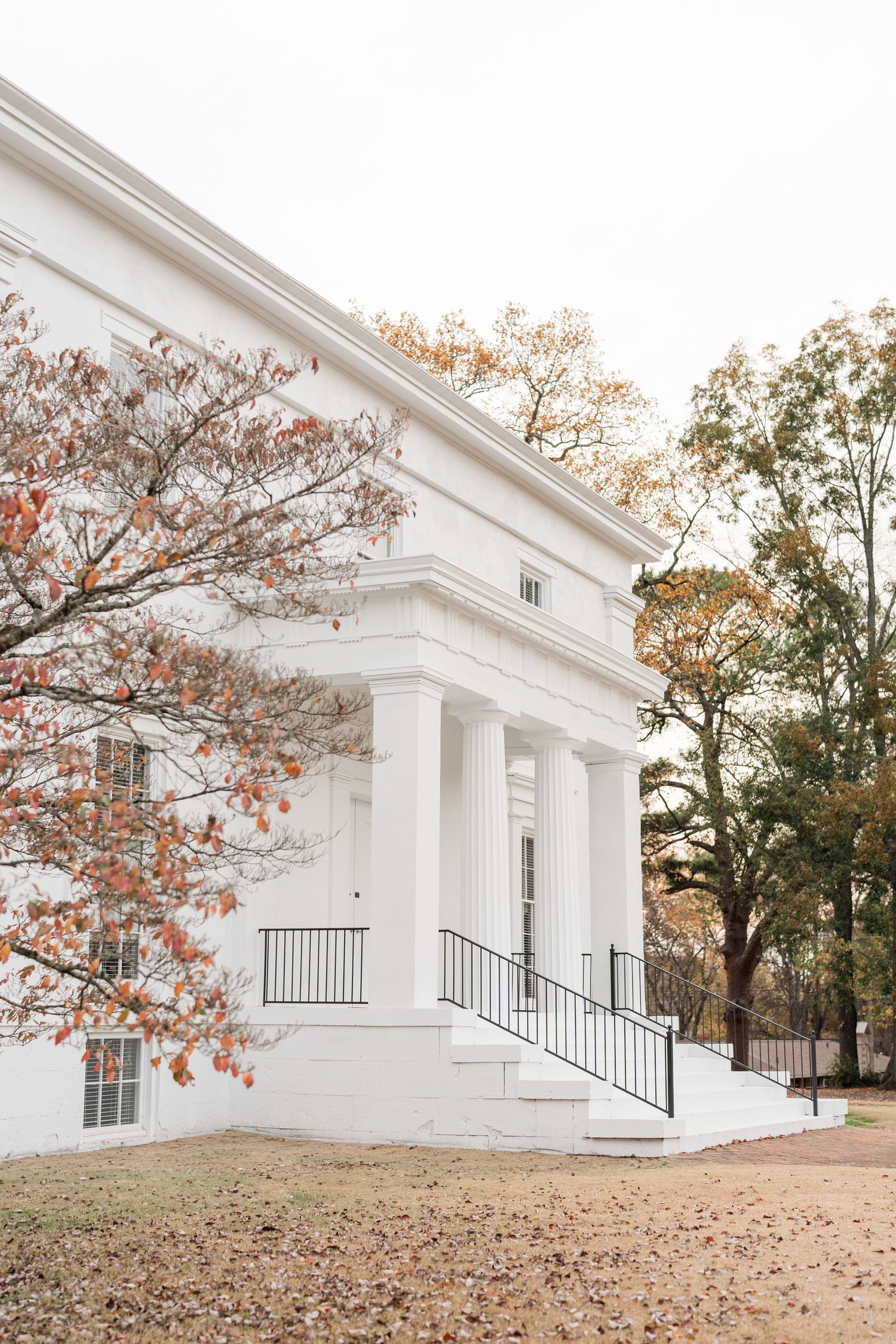 Classic white colonial building with columns and fall foliage in the background.