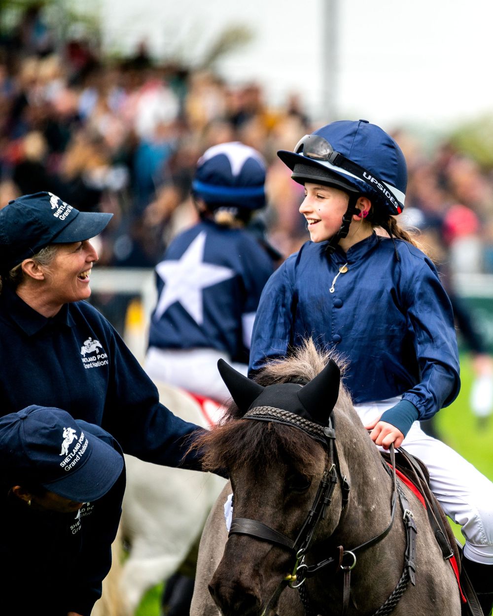 Smiling young rider in navy silks on a pony after finishing a Shetland Pony Grand National race.