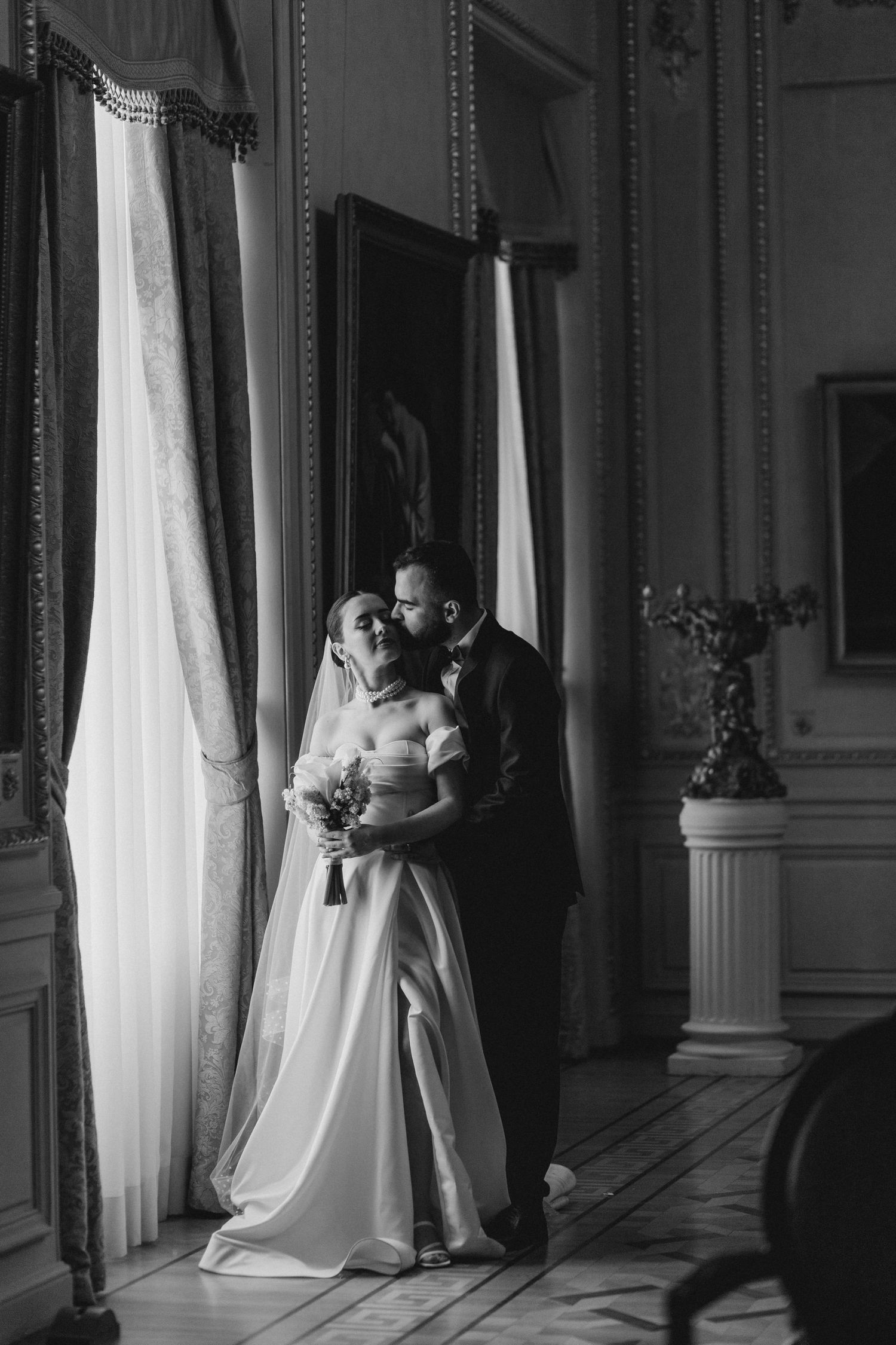 A tender black and white wedding moment by elegant floor-length windows.