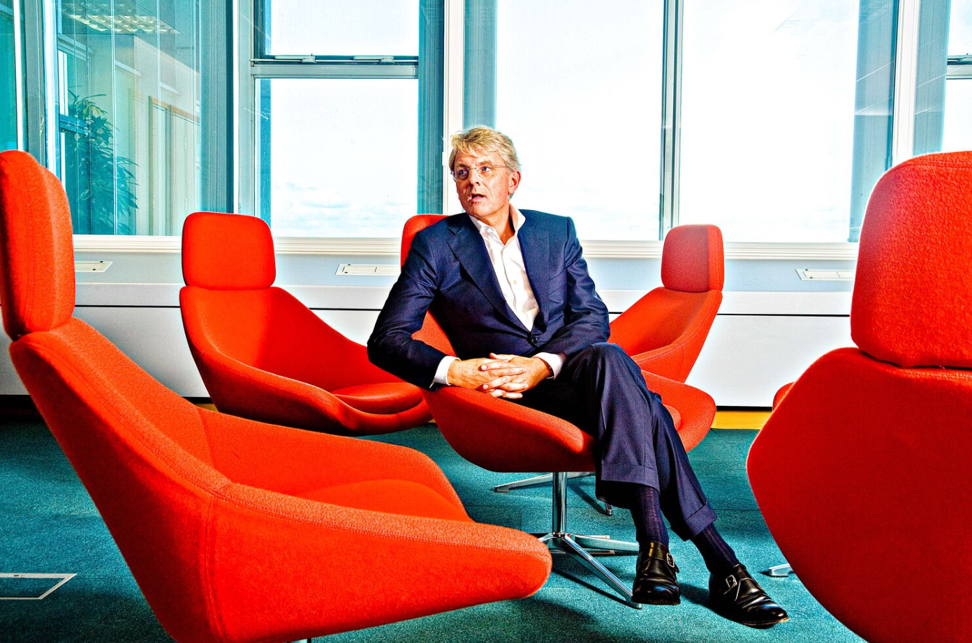 Professional seated in modern office space with bright red chairs and large windows.